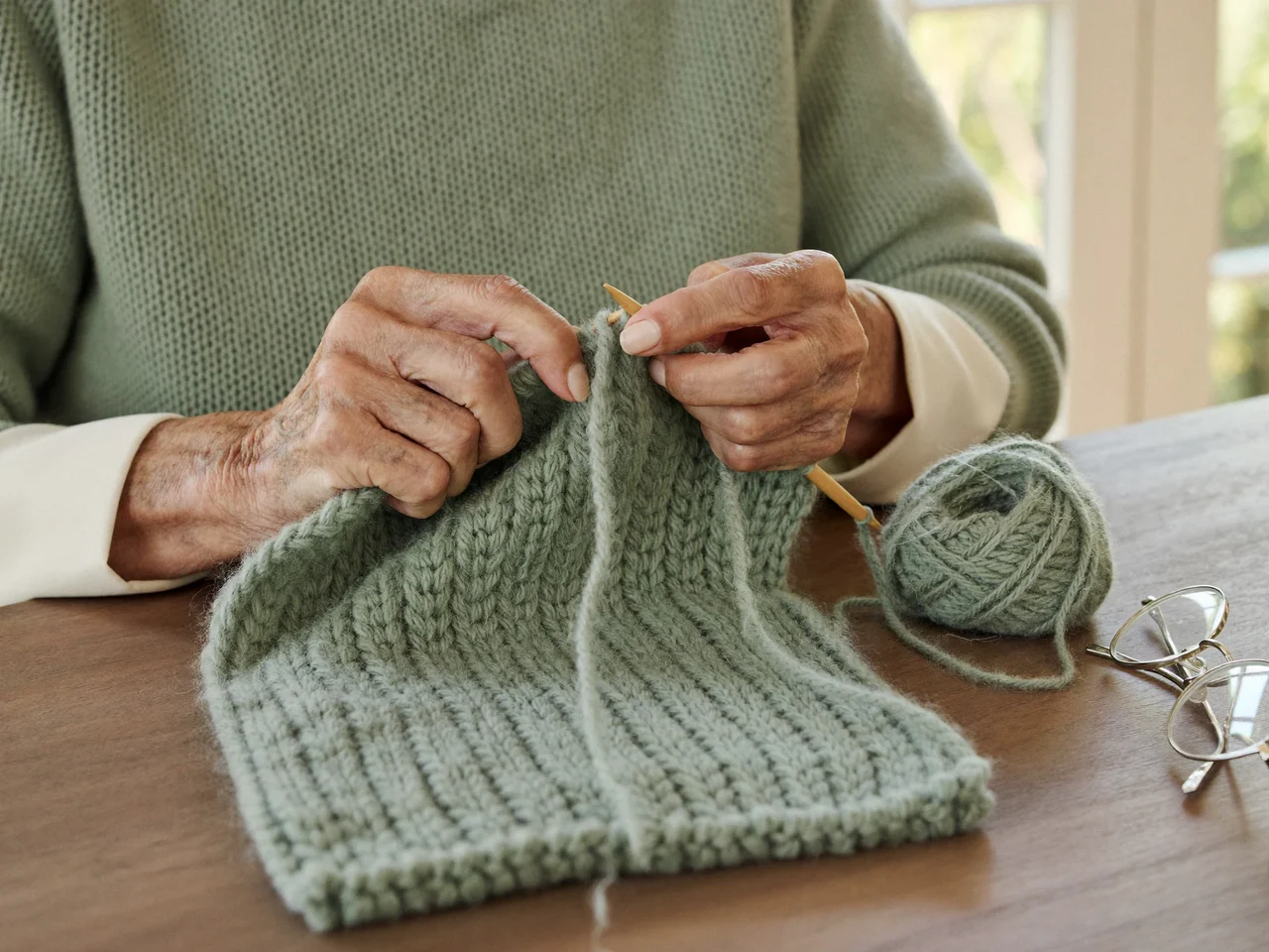 Mani di donna che lavorano a maglia una sciarpa verde salvia con ferri di legno.