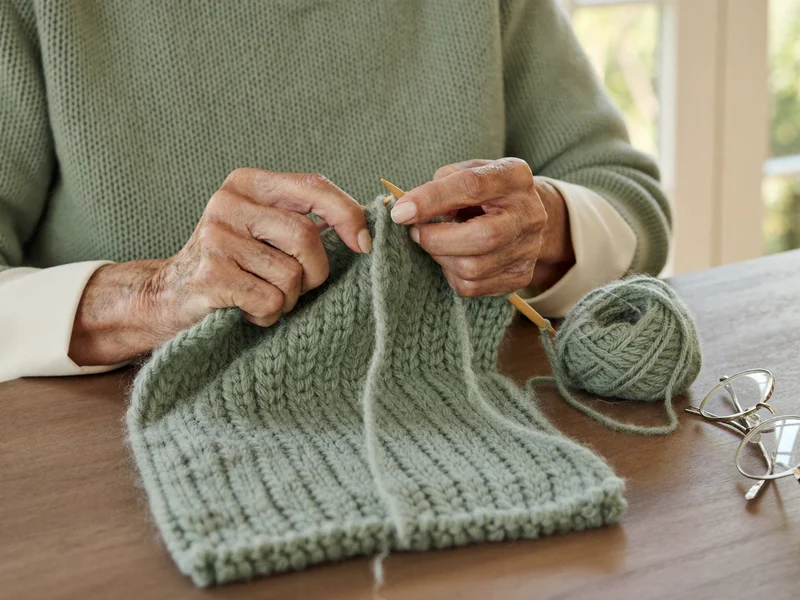 Mani di donna che lavorano a maglia una sciarpa verde salvia con ferri di legno.